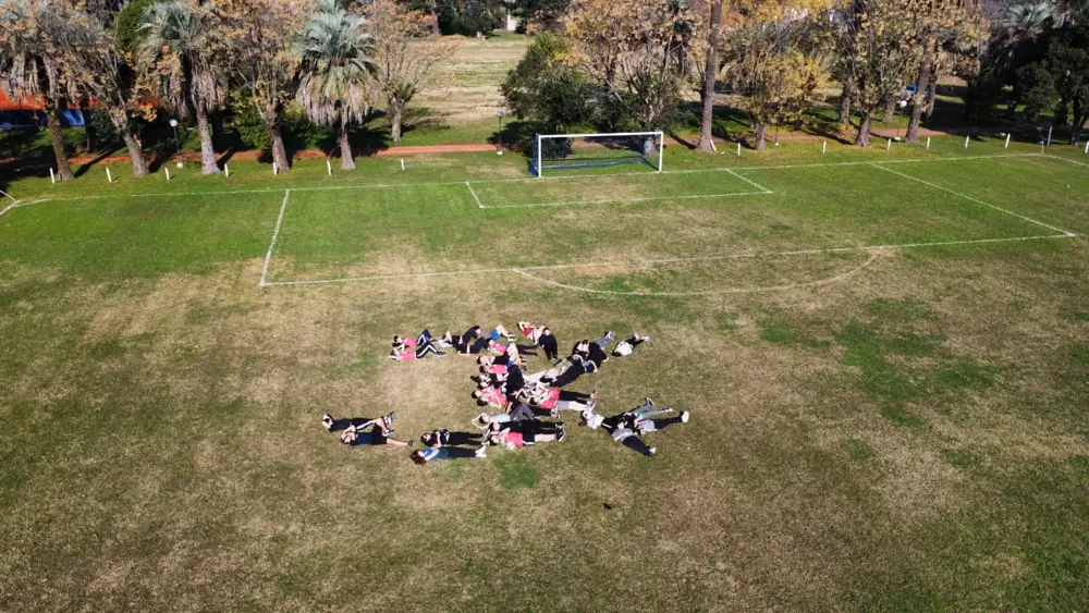 A group lying on the grass forming a shape, seen from a drone