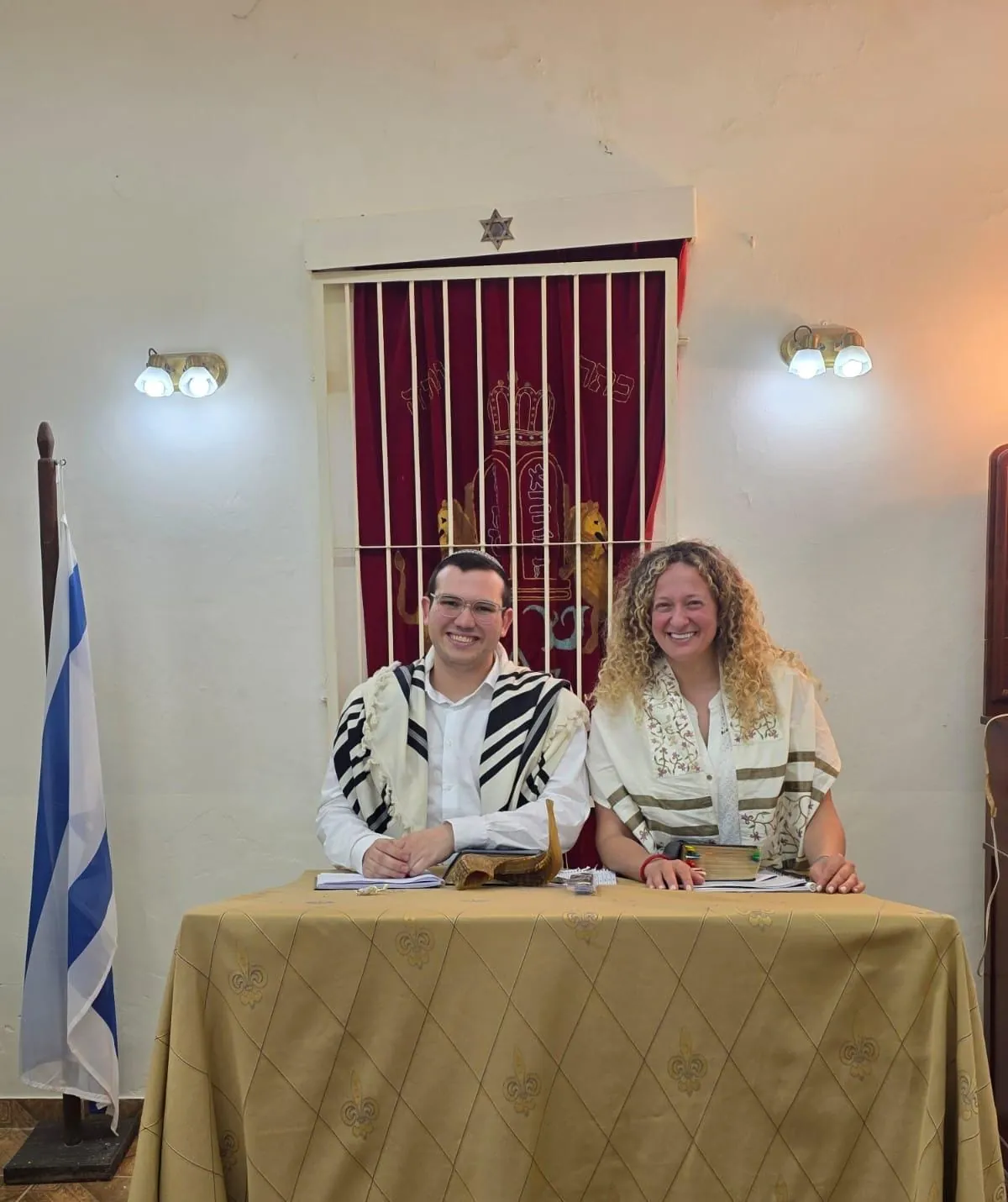 Mati and Bet Fleischer wearing tallitot, seated in front of the ark